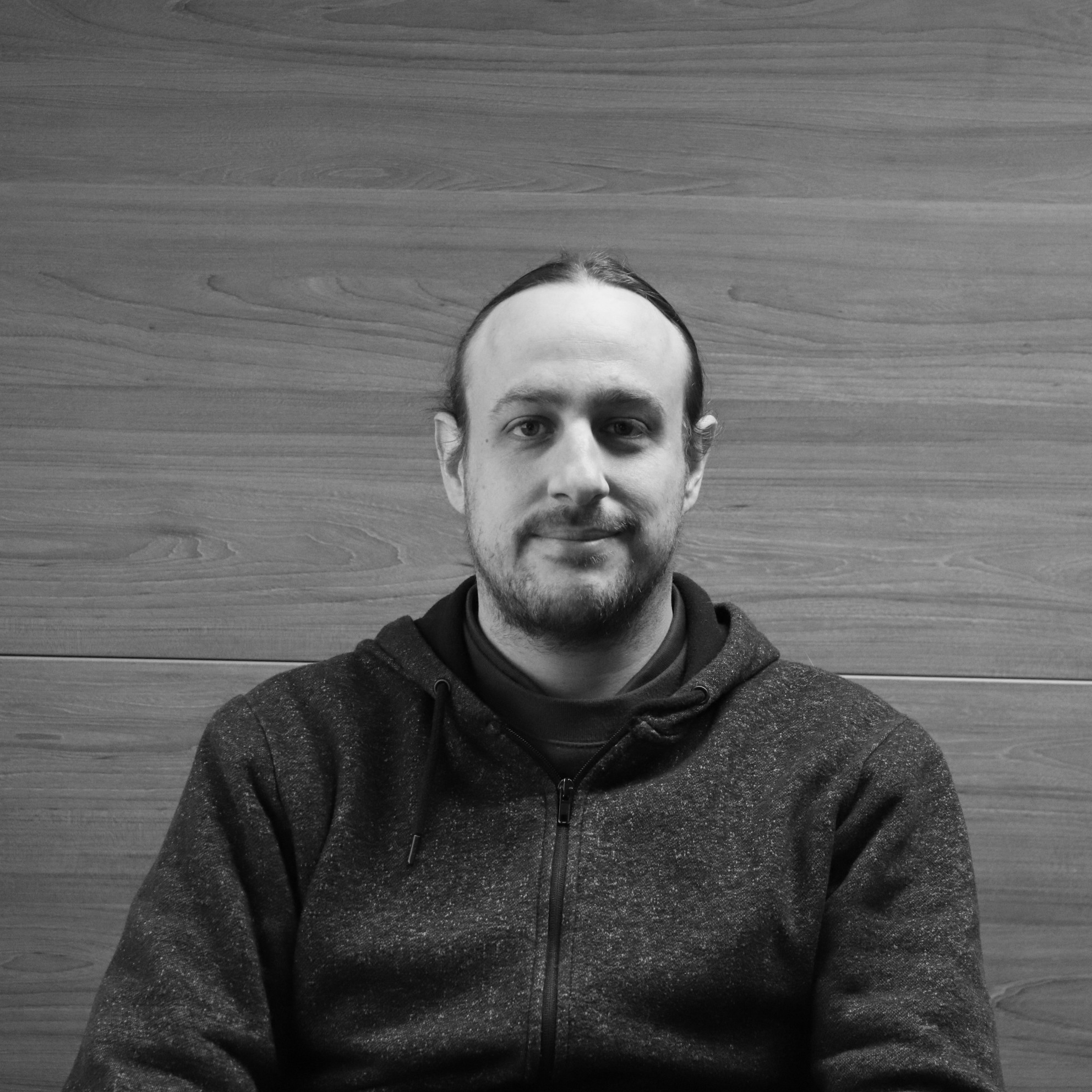 A black and white photo of MHT Technology Production Supervisor in front of wood panelled wall.