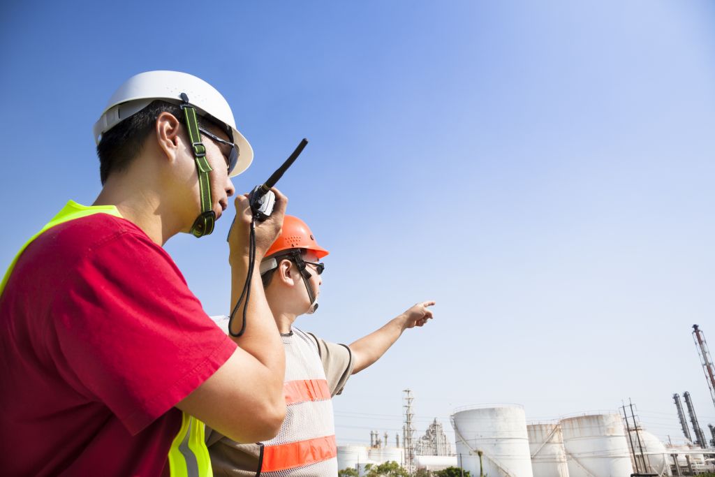 two refinery workers looking the large refinery background