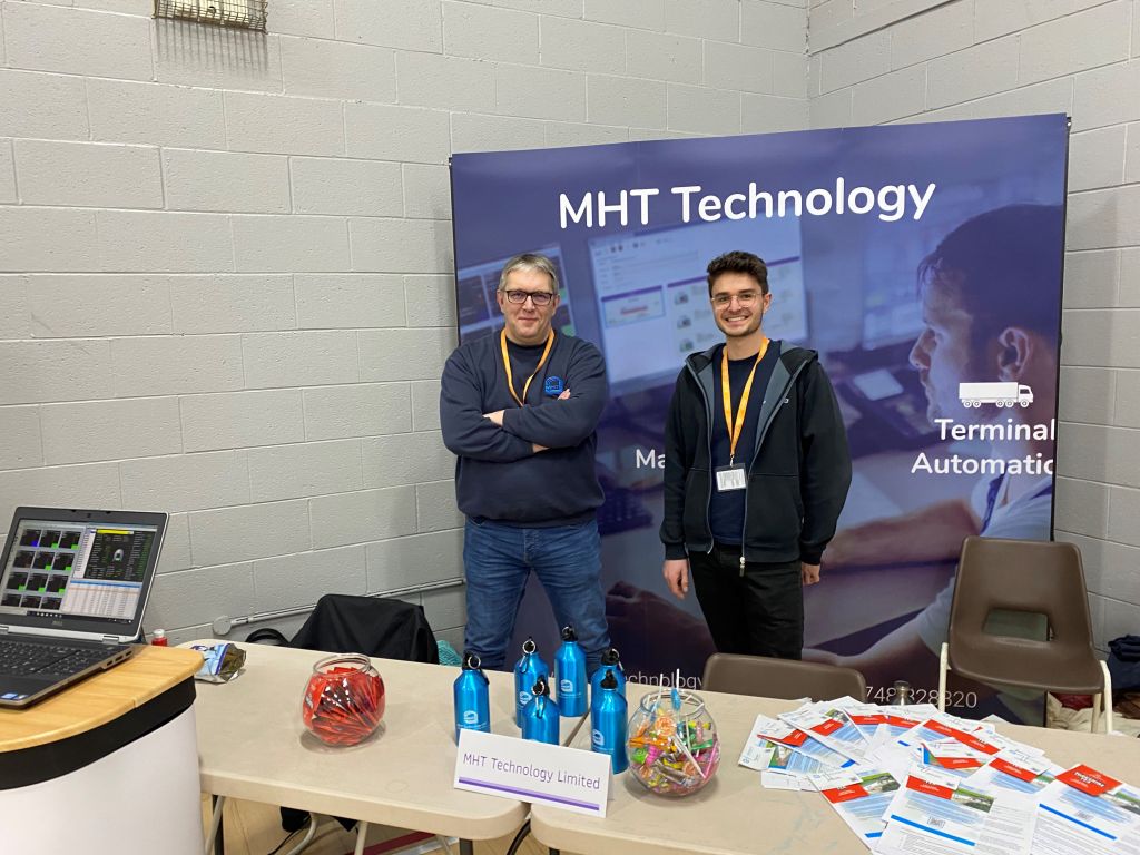 Two male MHT Technology colleagues stood at an exhibition stand during a school visit.